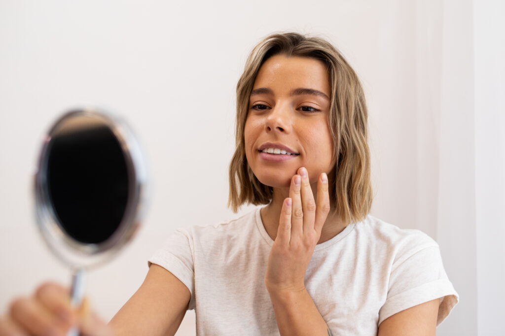 A woman uses a handheld mirror to look at her skin after her face mapping skin analysis near Red Oak, North Carolina, at Amazing Grace Aesthetics.